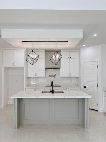 kitchen featuring pendant lighting, sink, white cabinets, light stone countertops, and a center island with sink