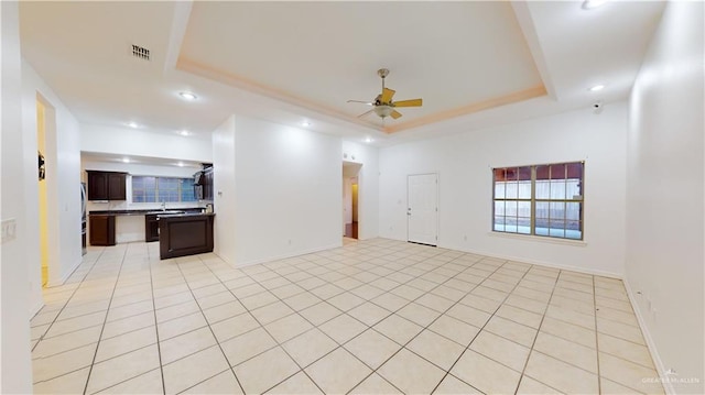 unfurnished living room featuring light tile patterned floors, a raised ceiling, ceiling fan, and sink