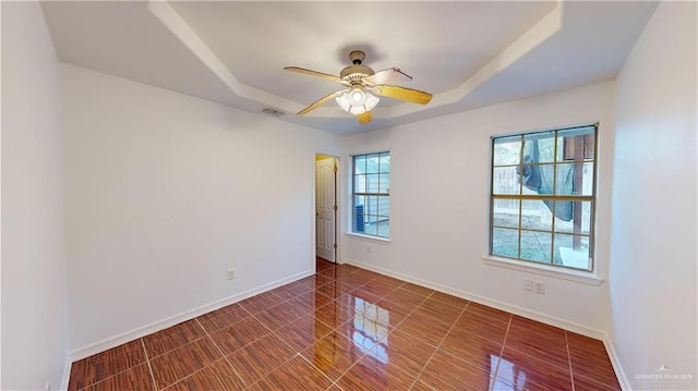 tiled spare room featuring a raised ceiling and ceiling fan