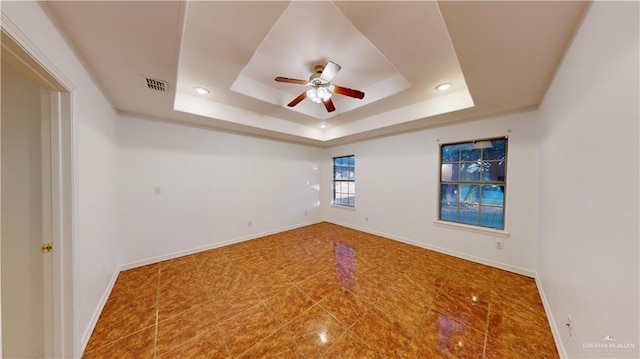 empty room featuring a raised ceiling, ceiling fan, and tile patterned flooring