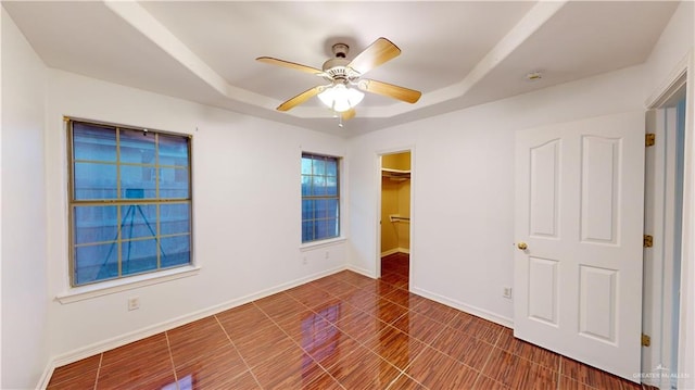 unfurnished bedroom featuring ceiling fan, a raised ceiling, a walk in closet, and a closet