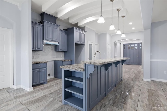 kitchen featuring pendant lighting, a kitchen bar, decorative backsplash, an island with sink, and light stone counters