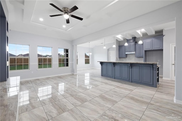 kitchen featuring light stone counters, a center island, decorative light fixtures, and ceiling fan with notable chandelier