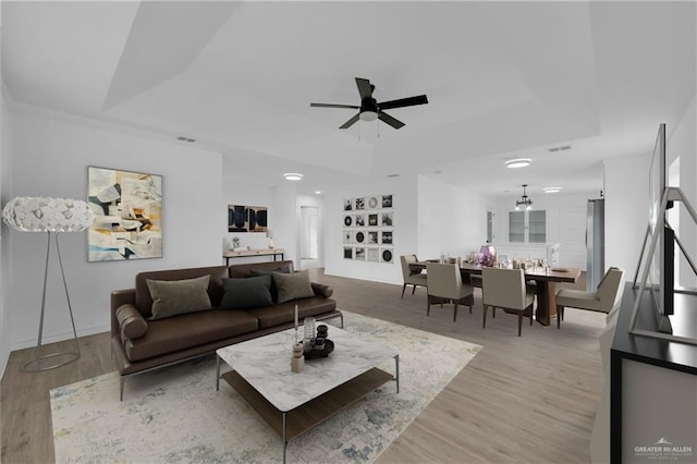 living room featuring built in shelves, ceiling fan, a raised ceiling, and light hardwood / wood-style flooring