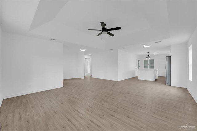 unfurnished living room with a tray ceiling, ceiling fan, and light wood-type flooring