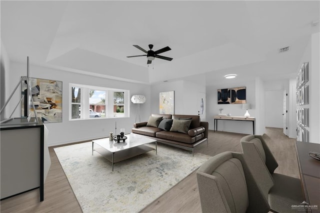 living room featuring light hardwood / wood-style flooring, ceiling fan, and a tray ceiling