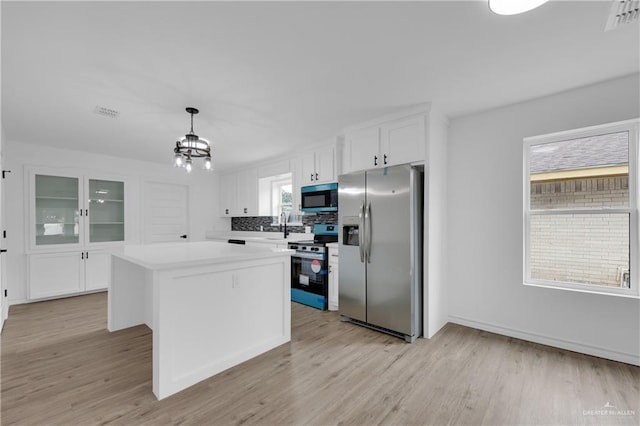 kitchen featuring a kitchen island, appliances with stainless steel finishes, white cabinets, hanging light fixtures, and an inviting chandelier