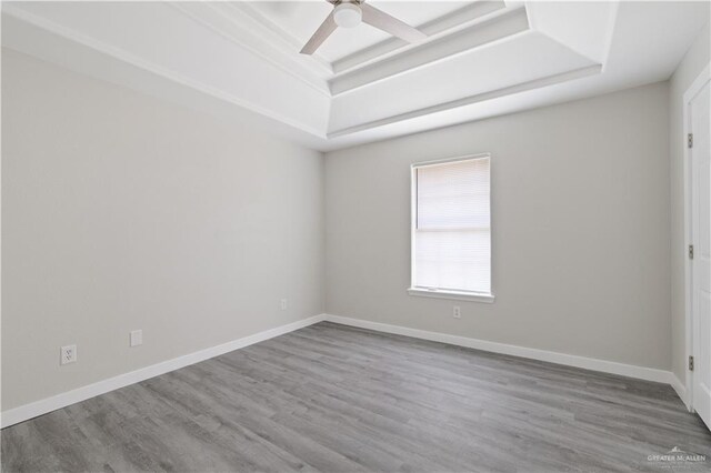 empty room featuring a tray ceiling, baseboards, and wood finished floors
