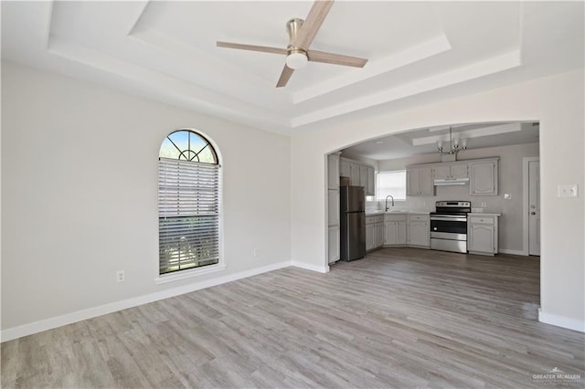 unfurnished living room with light wood finished floors, baseboards, and a raised ceiling
