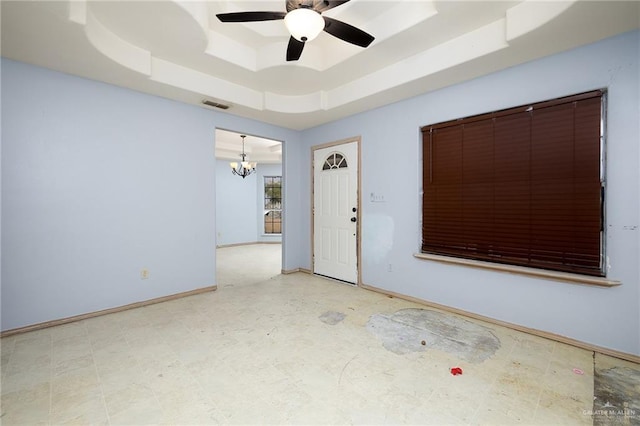 empty room with ceiling fan with notable chandelier and a raised ceiling