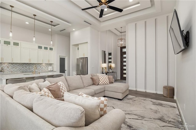 living room featuring a raised ceiling, sink, a towering ceiling, and ceiling fan with notable chandelier