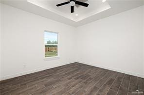 unfurnished room featuring a tray ceiling, dark wood finished floors, baseboards, recessed lighting, and a ceiling fan