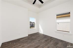 spare room with dark wood finished floors, ceiling fan, baseboards, and a raised ceiling