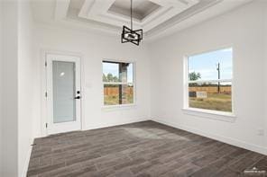 unfurnished dining area with a chandelier, dark wood finished floors, a healthy amount of sunlight, and coffered ceiling