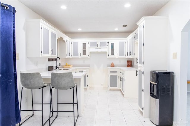 kitchen featuring kitchen peninsula, a breakfast bar, sink, light tile patterned floors, and white cabinets