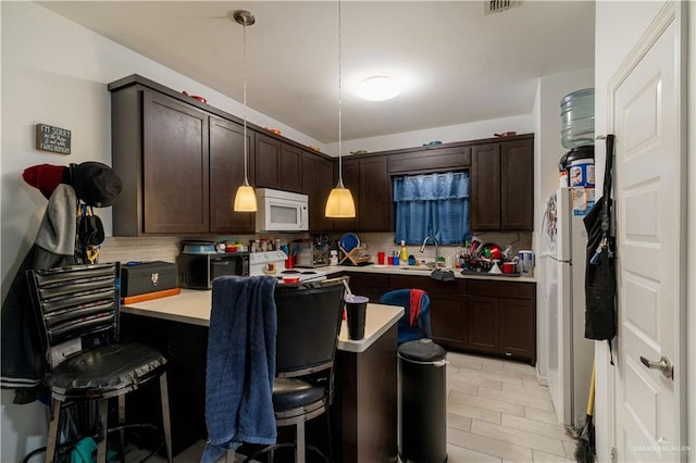 kitchen featuring white appliances, hanging light fixtures, tasteful backsplash, dark brown cabinetry, and a breakfast bar area