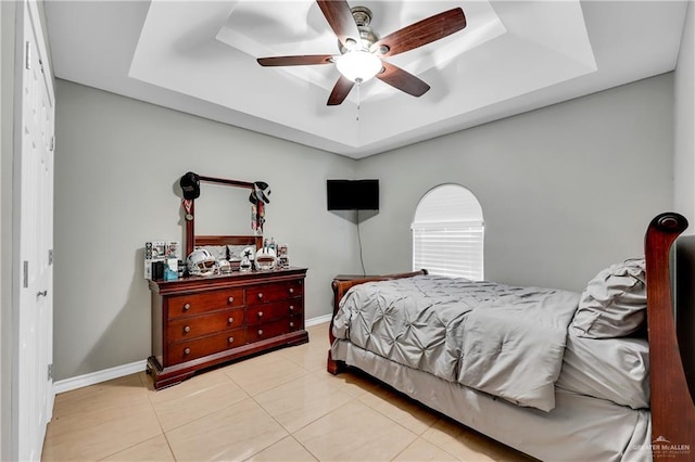 tiled bedroom featuring ceiling fan and a tray ceiling