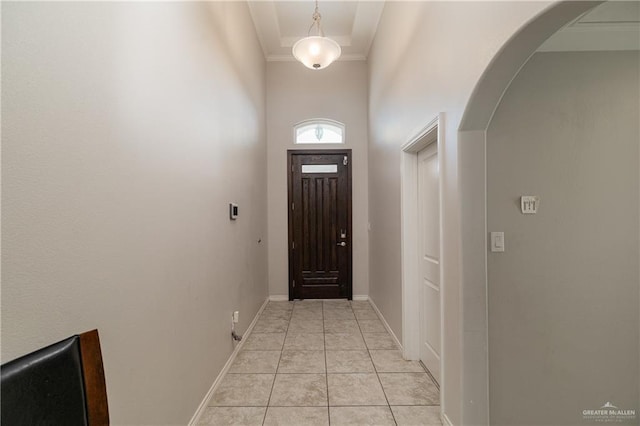 entryway featuring a high ceiling, light tile patterned floors, arched walkways, crown molding, and baseboards