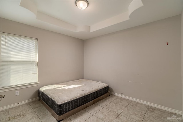 bedroom featuring a raised ceiling, baseboards, and light tile patterned floors