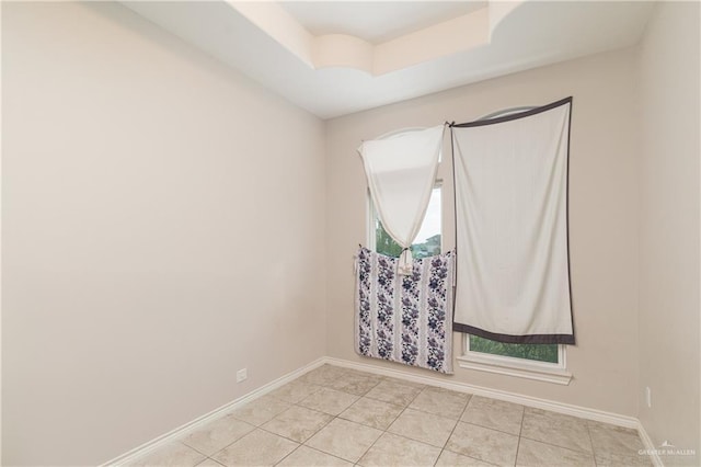 spare room with a raised ceiling, baseboards, and light tile patterned floors