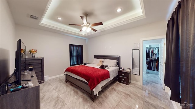 bedroom with a raised ceiling, a walk in closet, ceiling fan, and a closet