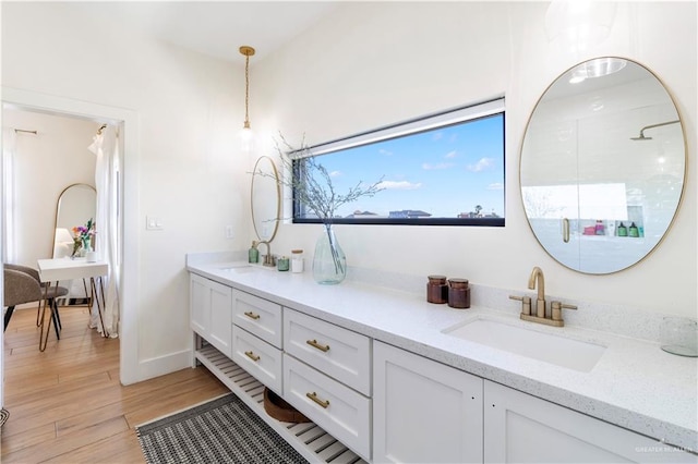 bathroom with double vanity, a shower with shower door, wood finished floors, and a sink