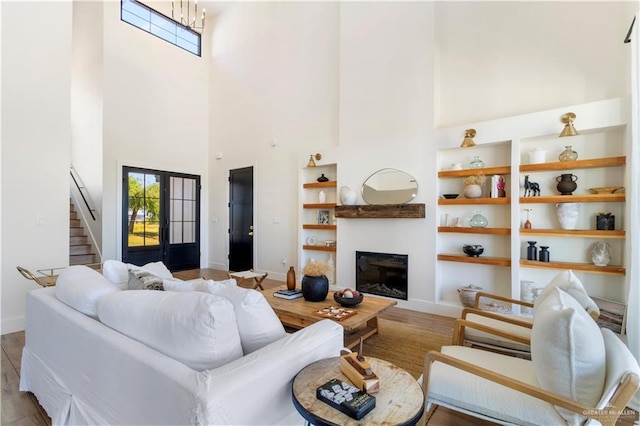 living area featuring built in shelves, baseboards, stairs, wood finished floors, and a glass covered fireplace