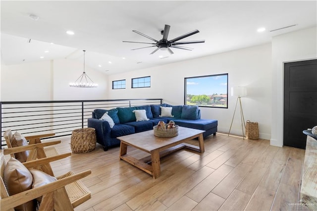 living room featuring vaulted ceiling, light wood-style flooring, recessed lighting, and ceiling fan with notable chandelier