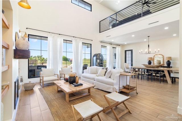 living room featuring light wood-style flooring, a high ceiling, recessed lighting, a glass covered fireplace, and a notable chandelier