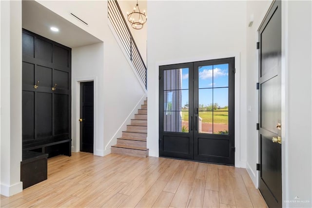 foyer entrance with stairs, light wood-style flooring, a notable chandelier, and french doors