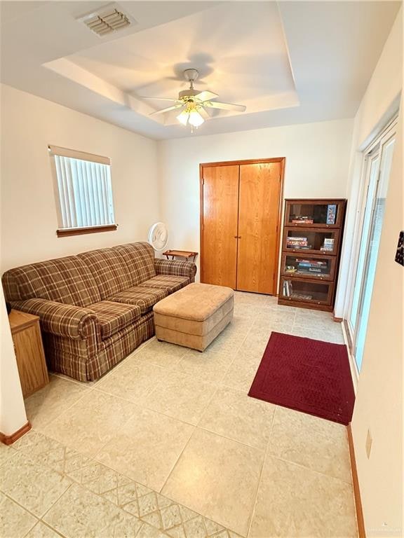 tiled living room with ceiling fan, a raised ceiling, and plenty of natural light