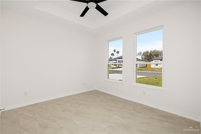 unfurnished room with a ceiling fan, a raised ceiling, and baseboards