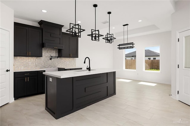 kitchen featuring a sink, backsplash, dark cabinetry, light countertops, and hanging light fixtures