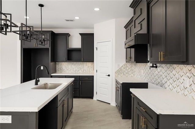 kitchen with visible vents, pendant lighting, an island with sink, decorative backsplash, and a sink