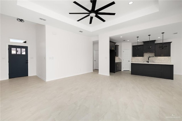 unfurnished living room featuring a sink, a tray ceiling, baseboards, and a ceiling fan