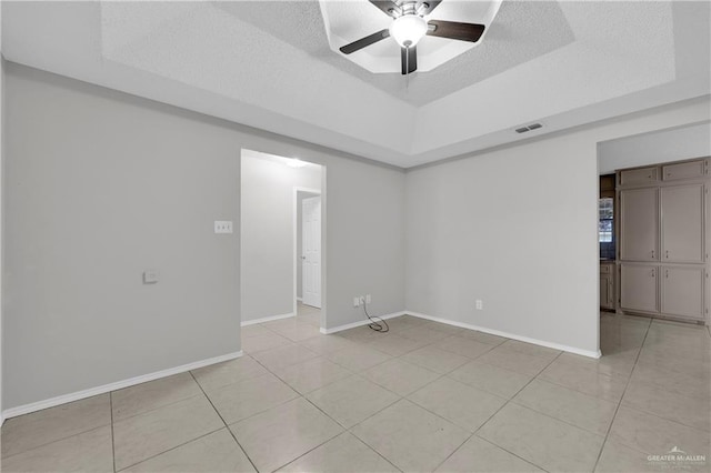 tiled spare room featuring ceiling fan, a tray ceiling, and a textured ceiling