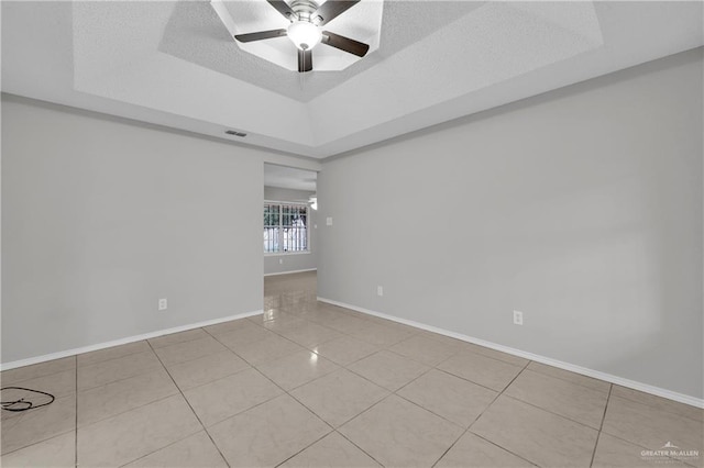 empty room with a raised ceiling, light tile patterned floors, a textured ceiling, and ceiling fan