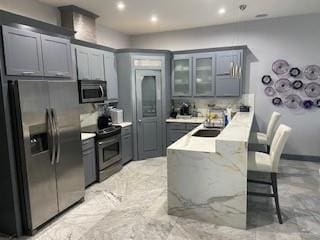 kitchen with appliances with stainless steel finishes, a kitchen breakfast bar, light stone counters, gray cabinetry, and sink