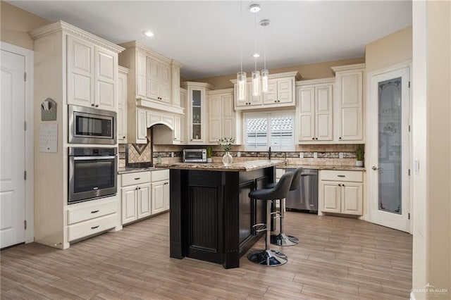 kitchen featuring a center island, stainless steel appliances, pendant lighting, light hardwood / wood-style floors, and a kitchen bar