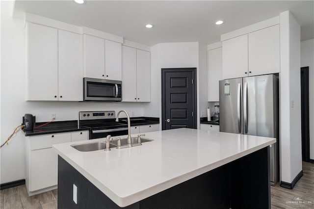 kitchen featuring appliances with stainless steel finishes, a kitchen island with sink, sink, light hardwood / wood-style flooring, and white cabinets