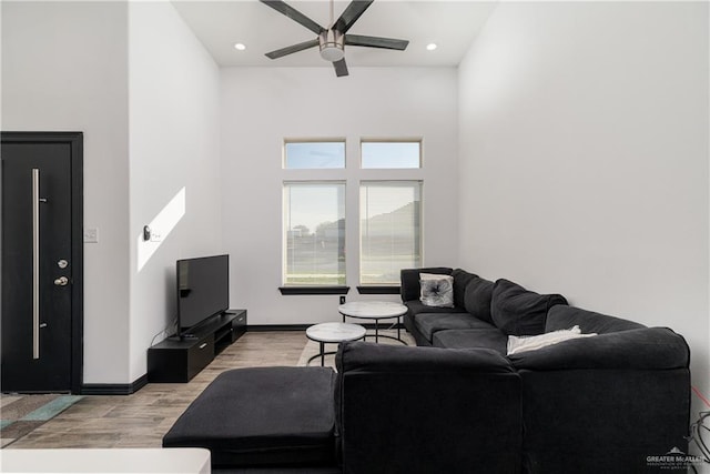 living room featuring ceiling fan, light hardwood / wood-style floors, and a high ceiling