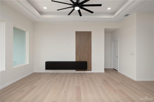 empty room featuring visible vents, ceiling fan, a raised ceiling, baseboards, and light wood-style floors