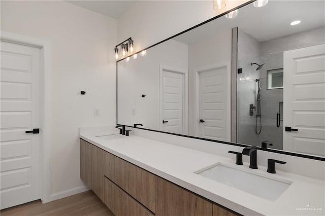 bathroom with a shower stall, double vanity, a sink, and wood finished floors