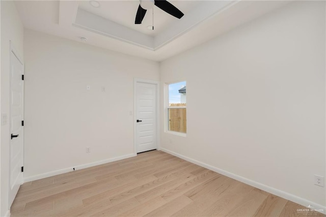 spare room featuring a tray ceiling, light wood-style flooring, baseboards, and ceiling fan
