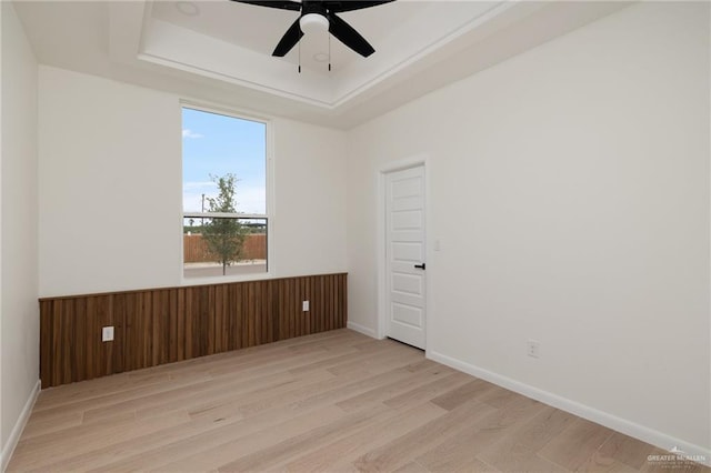 empty room with baseboards, wood finished floors, a raised ceiling, and ceiling fan