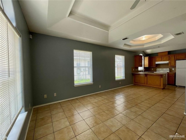 kitchen with under cabinet range hood, a peninsula, visible vents, freestanding refrigerator, and a tray ceiling