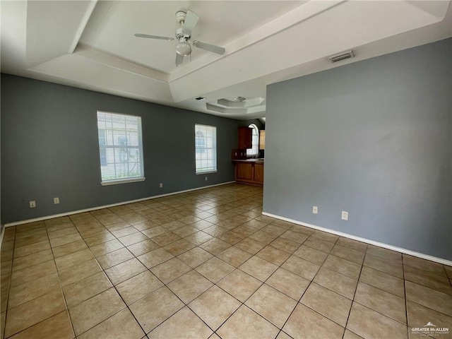 unfurnished room with light tile patterned floors, visible vents, baseboards, a ceiling fan, and a tray ceiling