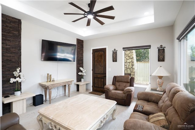 living room with a tray ceiling, plenty of natural light, and ceiling fan