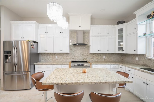 kitchen featuring stainless steel appliances, hanging light fixtures, wall chimney exhaust hood, and a breakfast bar area