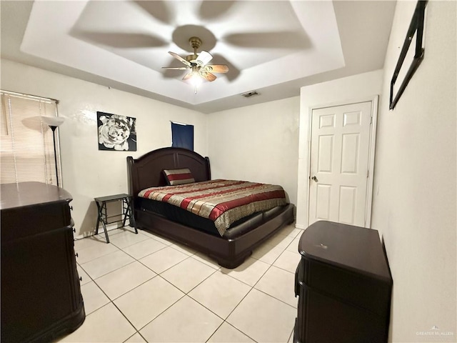 bedroom with ceiling fan, light tile patterned floors, and a tray ceiling